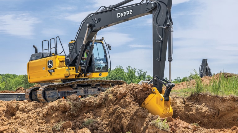 Una Excavadora 200G recoge tierra y césped en un lugar de trabajo.