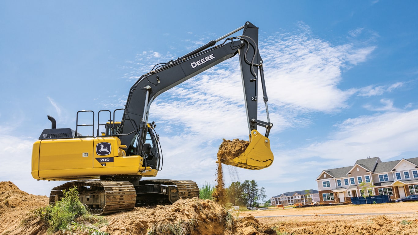 A 200G Excavator moving dirt at a worksite with a housing development in the background.