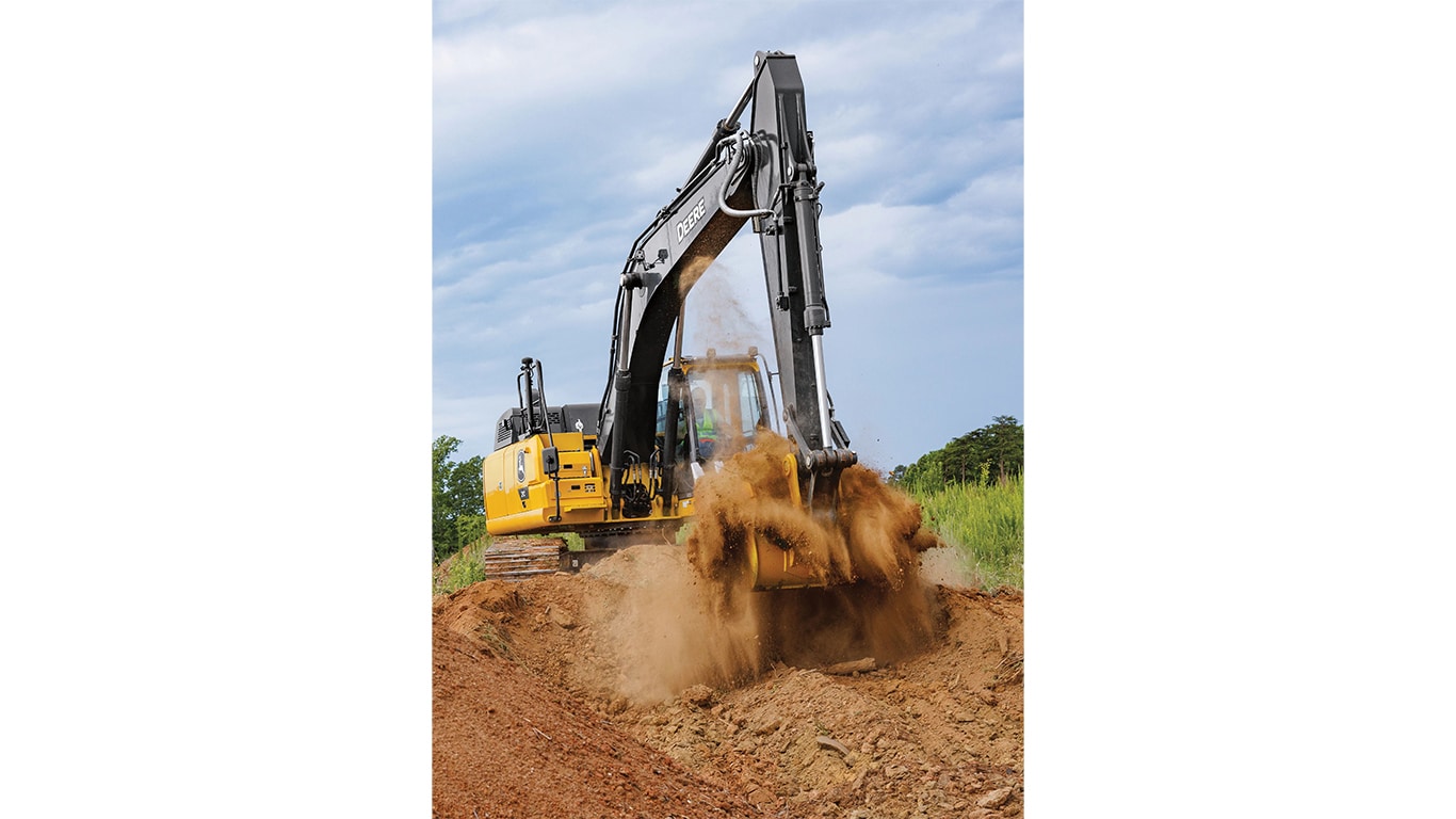 An operator using a 210P-Tier Excavator to move dirt with a green field and trees in the background.