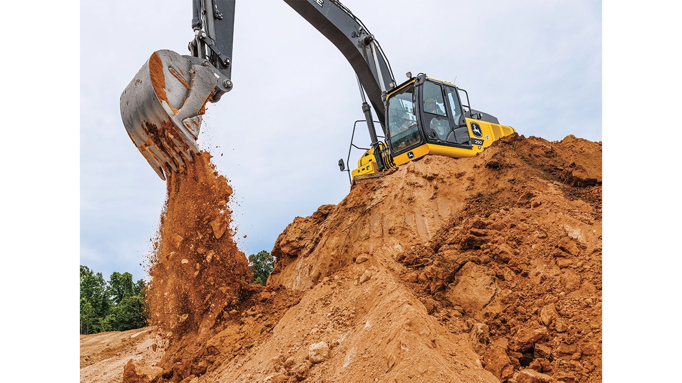 A 250P-Tier Excavator dumping dirt into a pit from the top of a stockpile.