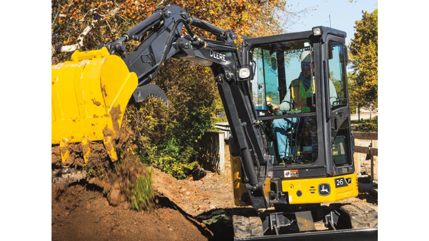 An operator using a 26P-Tier Excavator to dump dirt onto a pile in front of a fence.