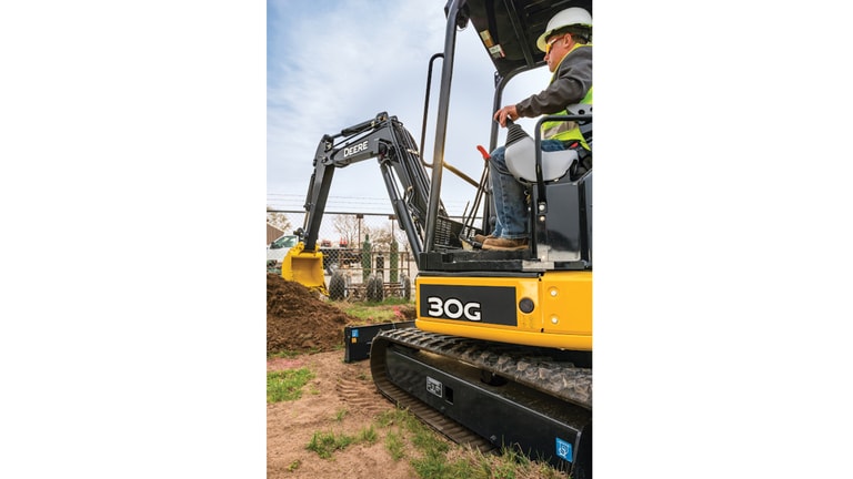 Operator using a 30G excavator to move topsoil in front of a fence.