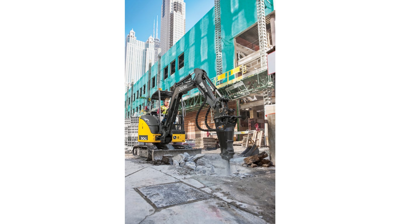 An operator using a 30G Excavator with an HH60C hammer attachment to break up concrete at a worksite.