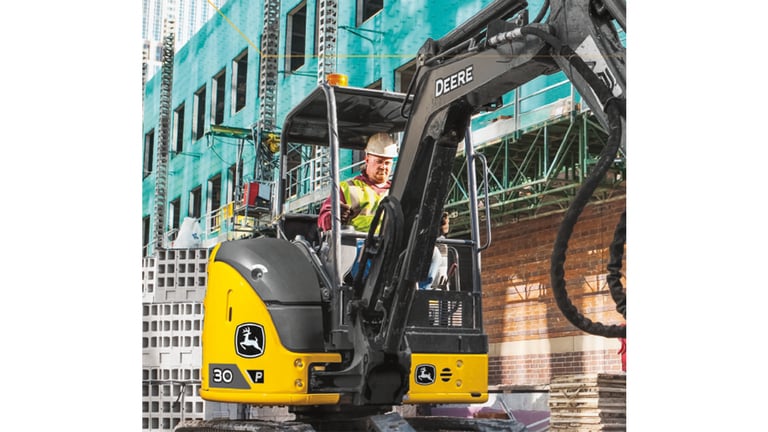 A close-up of an operator using a 30P-Tier Excavator at a worksite with buildings under construction in the background.
