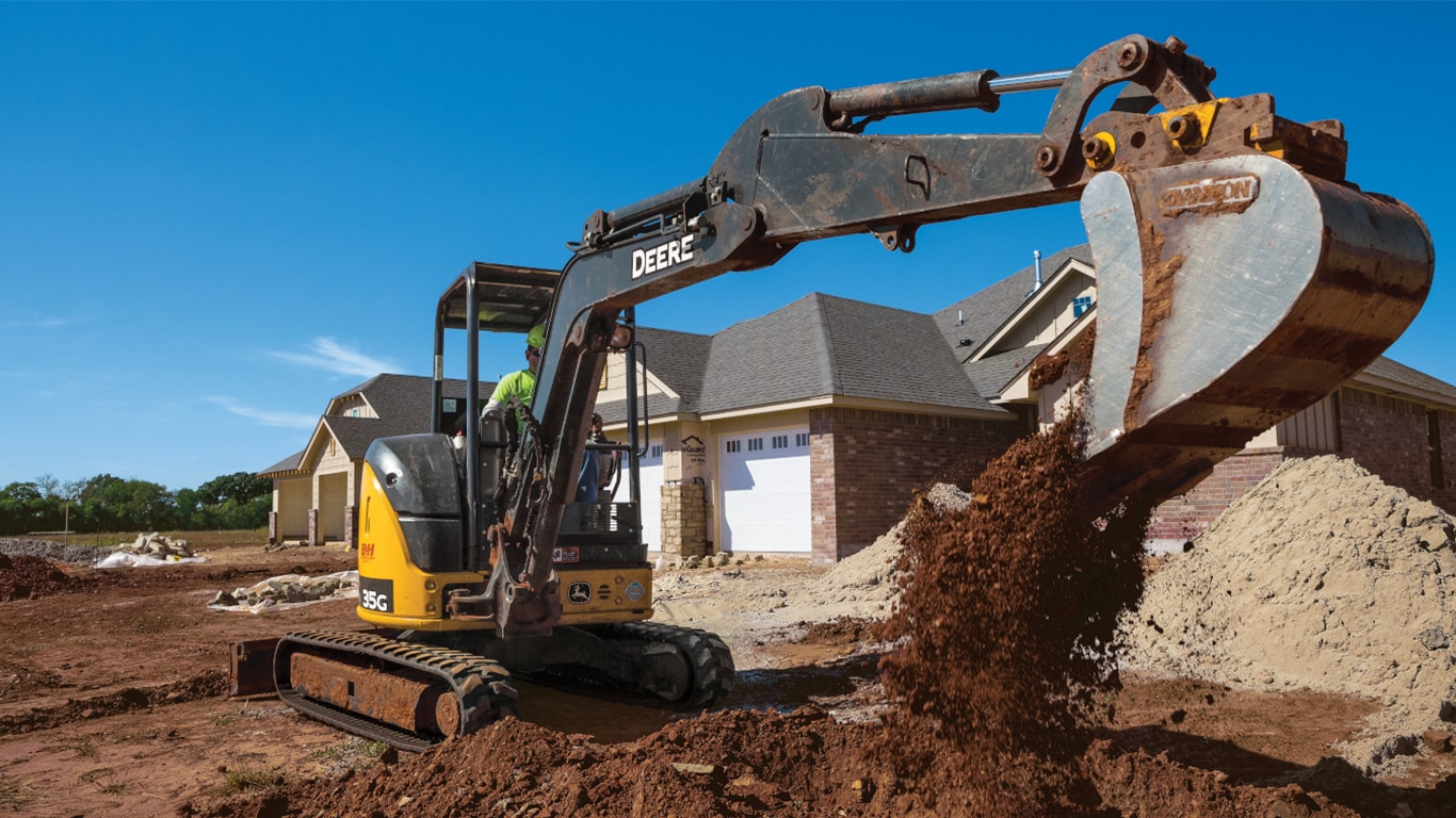 A 35G Excavator dumps topsoil into a pile in front of a housing development