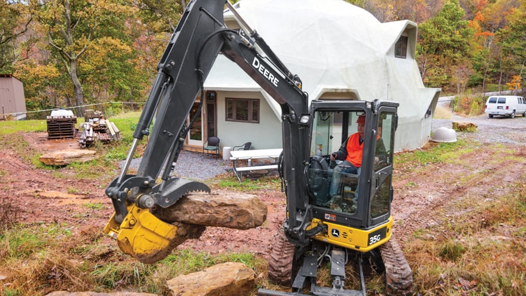 A man using a 35G Excavator to move large rocks in front of a house.