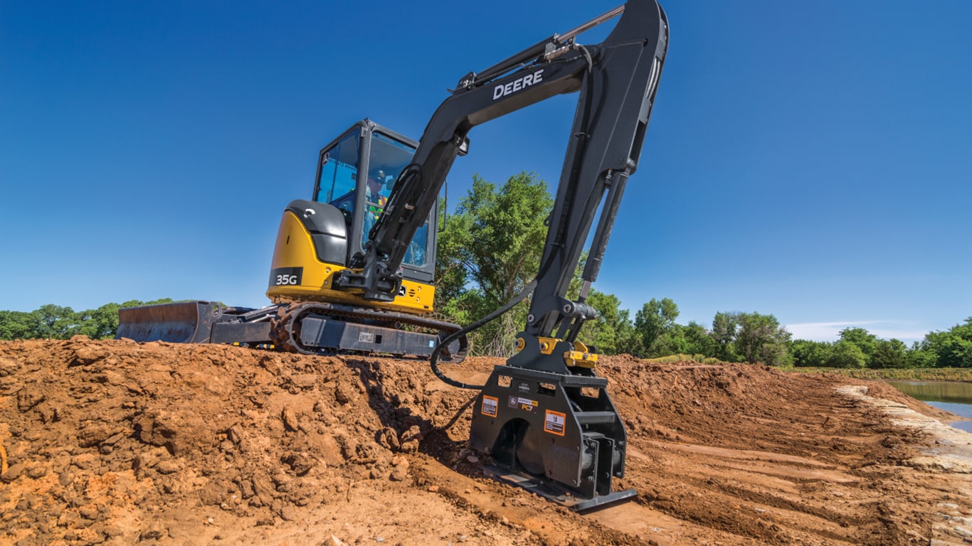  Compact Excavator Model 35G using a motorized tamper to flatten the dirt next to a pond