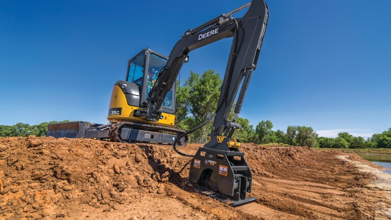 A 35G Excavator with a PC7 plate compactor attachment compacting dirt on a worksite.