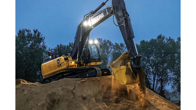A 380P-Tier Excavator with headlights moving dirt at dusk.