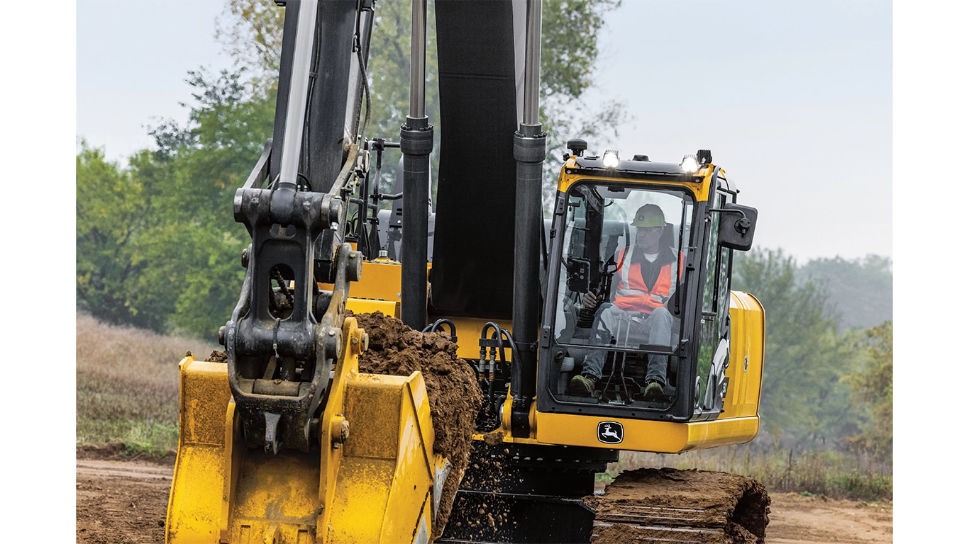 An operator using a 380P-Tier Excavator to move dirt at a worksite with trees in the background.