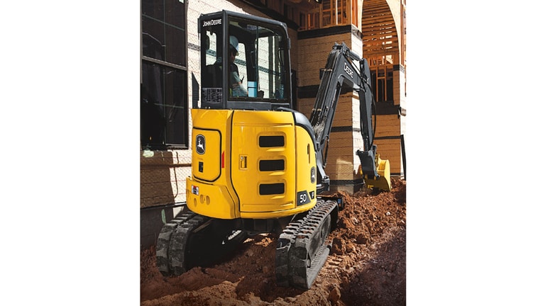 The back side of a 50 P-Tier Excavator moving dirt at a worksite with a building in the background.