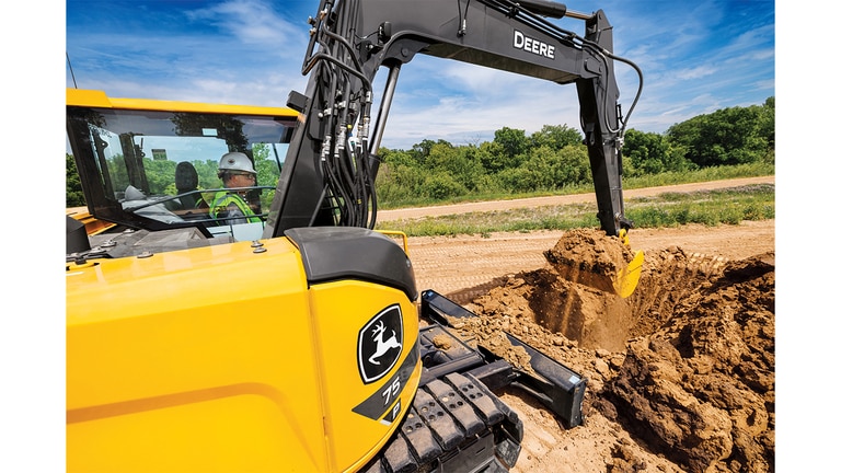 A close-up of a 75P-Tier Excavator scooping dirt at a worksite.