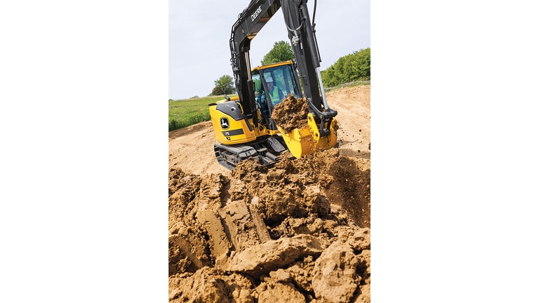 An operator using a 75P-Tier Excavator to scoop dirt at a worksite with grass and trees in the background.