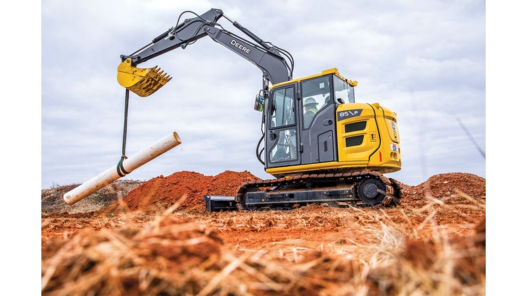 An 85P-Tier Excavator lowering pipe onto the ground at a worksite.