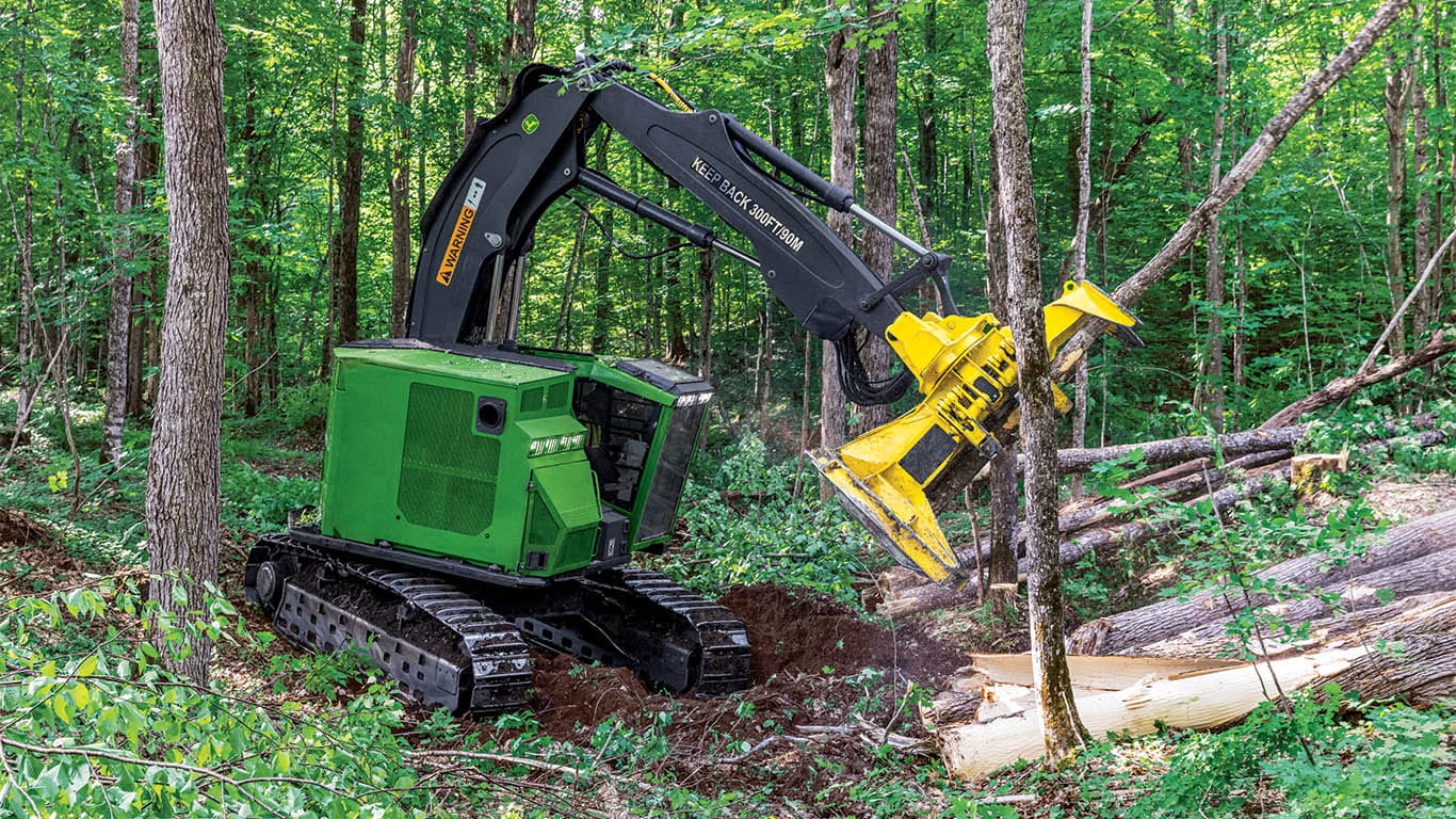 A John&nbsp;Deere wheeled feller buncher delimbing logs in a forest. 