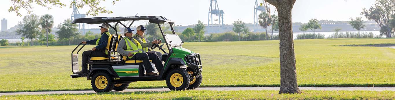 Three workers on a Gator Utility Vehicle at a work site—one driving, two riding.