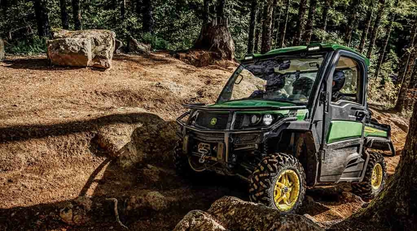 a XUV835M Gator off-roading over rocks in dense woods