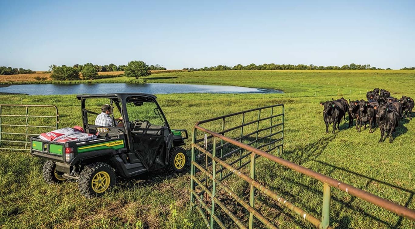 A person driving his XUV835M Gator into his cow pasture.