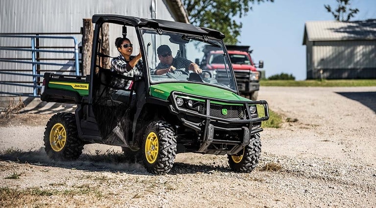 Two people riding in a XUV835M Gator on a gravel lot.