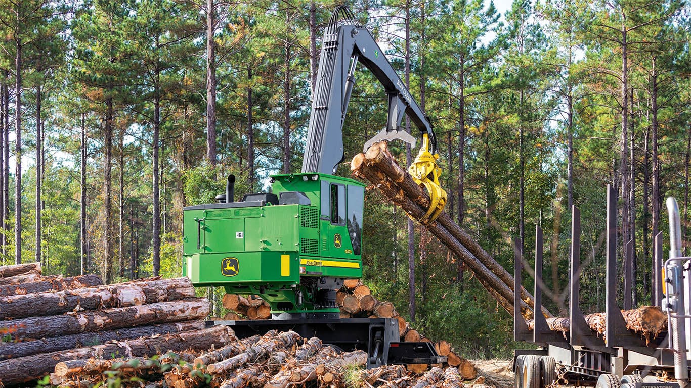 A John&nbsp;Deere knuckleboom loader prepares to add logs to the bed of a logging truck.