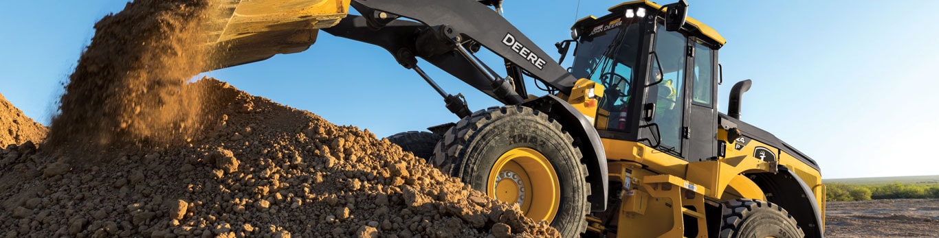 John&nbsp;Deere loader scoops dirt from a pile, showcasing its powerful front bucket and large tires.