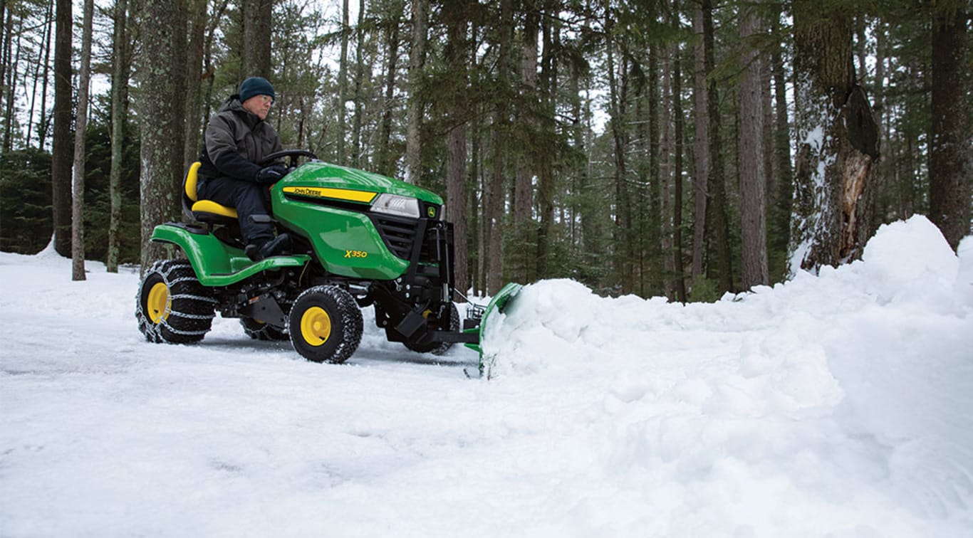A person using his X350 Mower with a Snowplow attachment to clear snow off the ground.