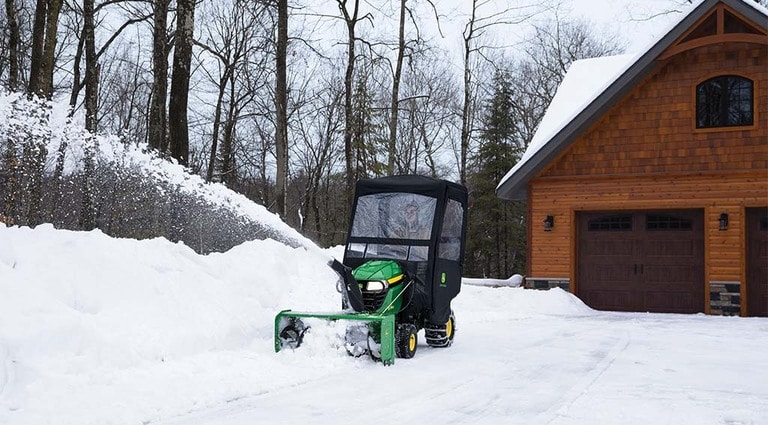 A person using their X350 Mower with a snowblower attachment to clear their snowy driveway.