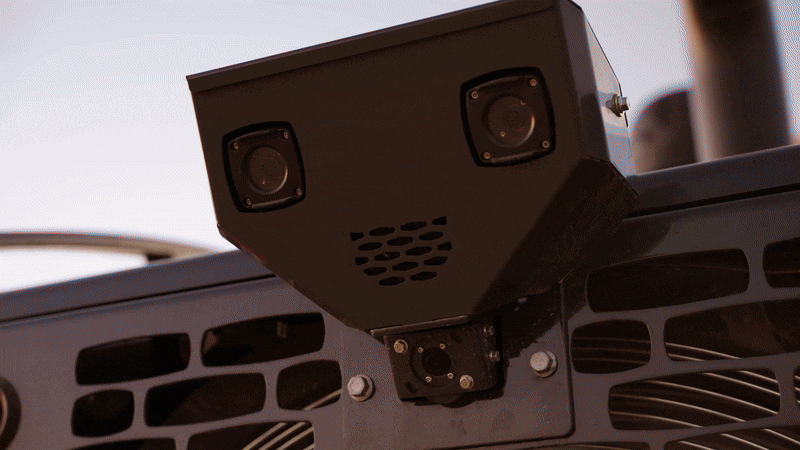 Close-up of a black, box-shaped camera with two lenses and ventilation holes mounted on a structure.