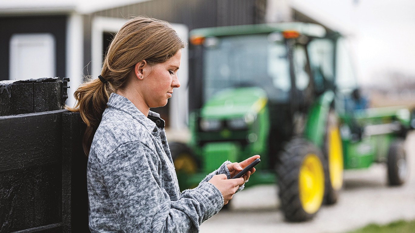 Woman with cell phone in hand and utility tractor in the background. 