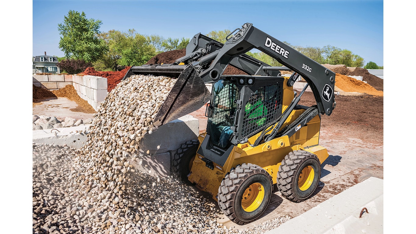 A 332G Skid Steer dumping rocks at a worksite.