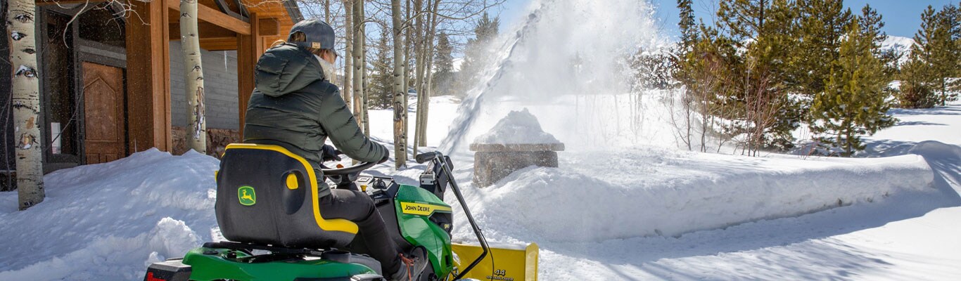 Woman riding a 100 series lawn tractor blowing snow with a snowblower