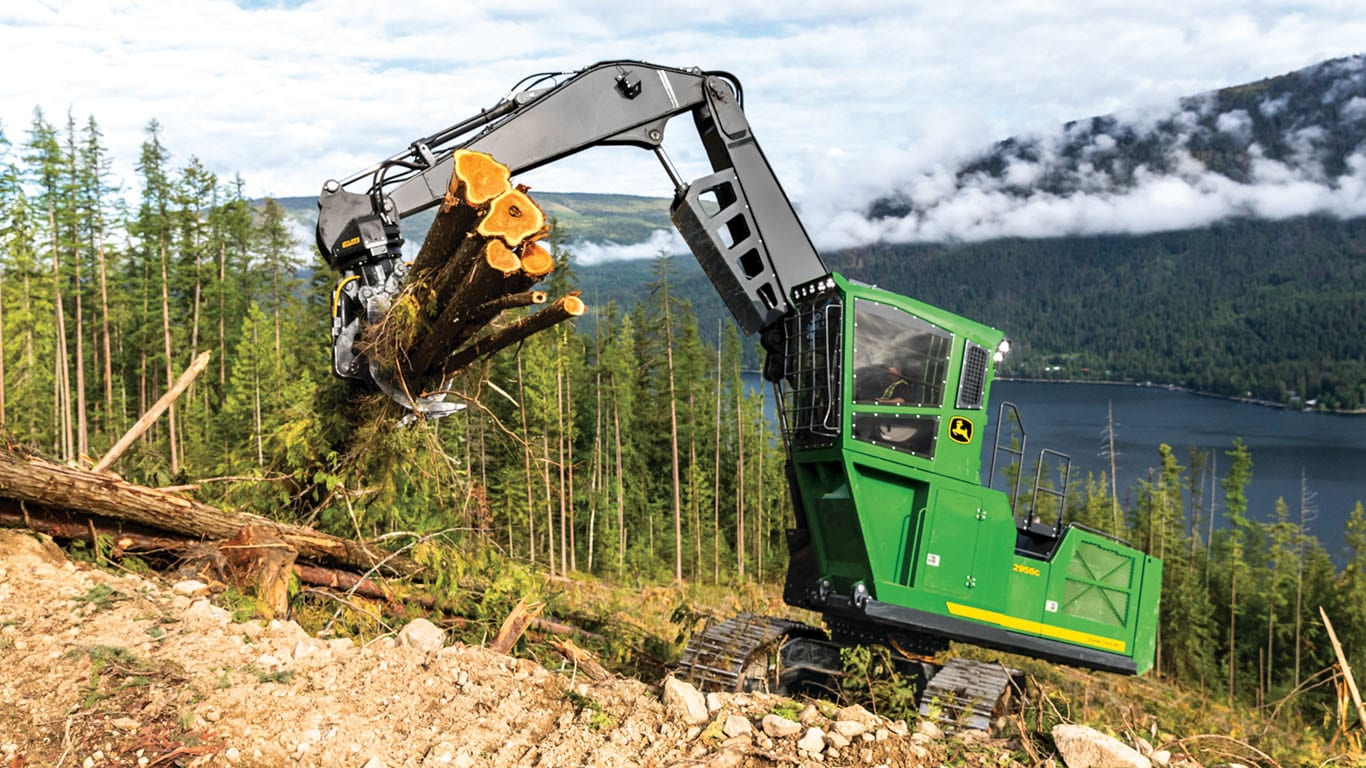 A John&nbsp;Deere swing machine lifting logs with lake and trees in the background.