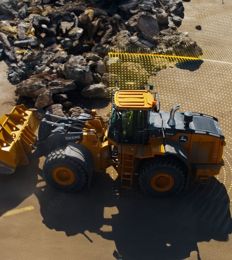 A large yellow John Deere 844 wheel loader moves rocks on a construction site, with a grid overlay showing its path.