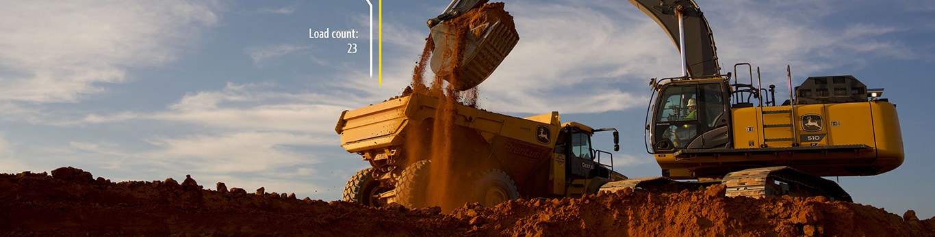 Excavator loading dirt into a dump truck at a construction site under a blue sky with clouds.