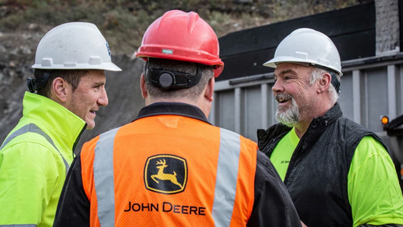 Two men talking to each other wearing a John Deere logo safety vest and hard hat
