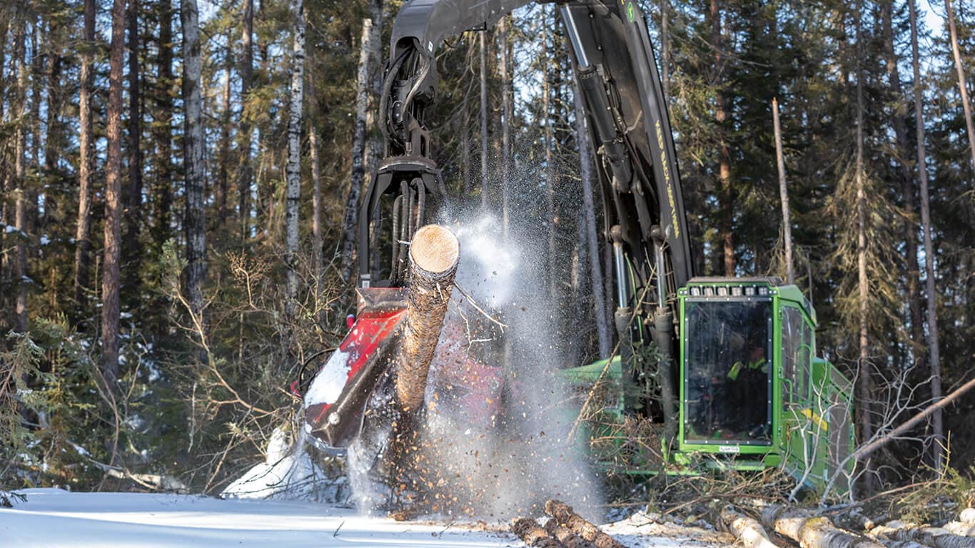John Deere tracked harvester working in snowy woods cutting logs to length. 