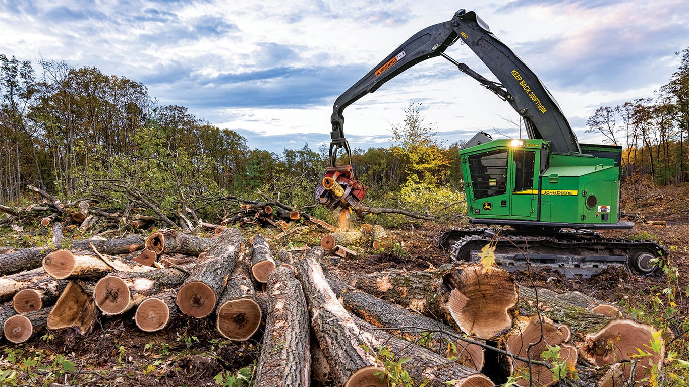 A John Deere tracked harvester dropping a log in a pile of logs.