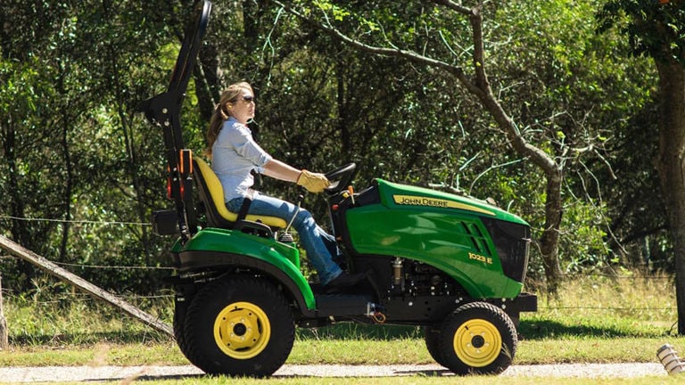 Woman driving a 1023E Compact Tractor down a dirt road