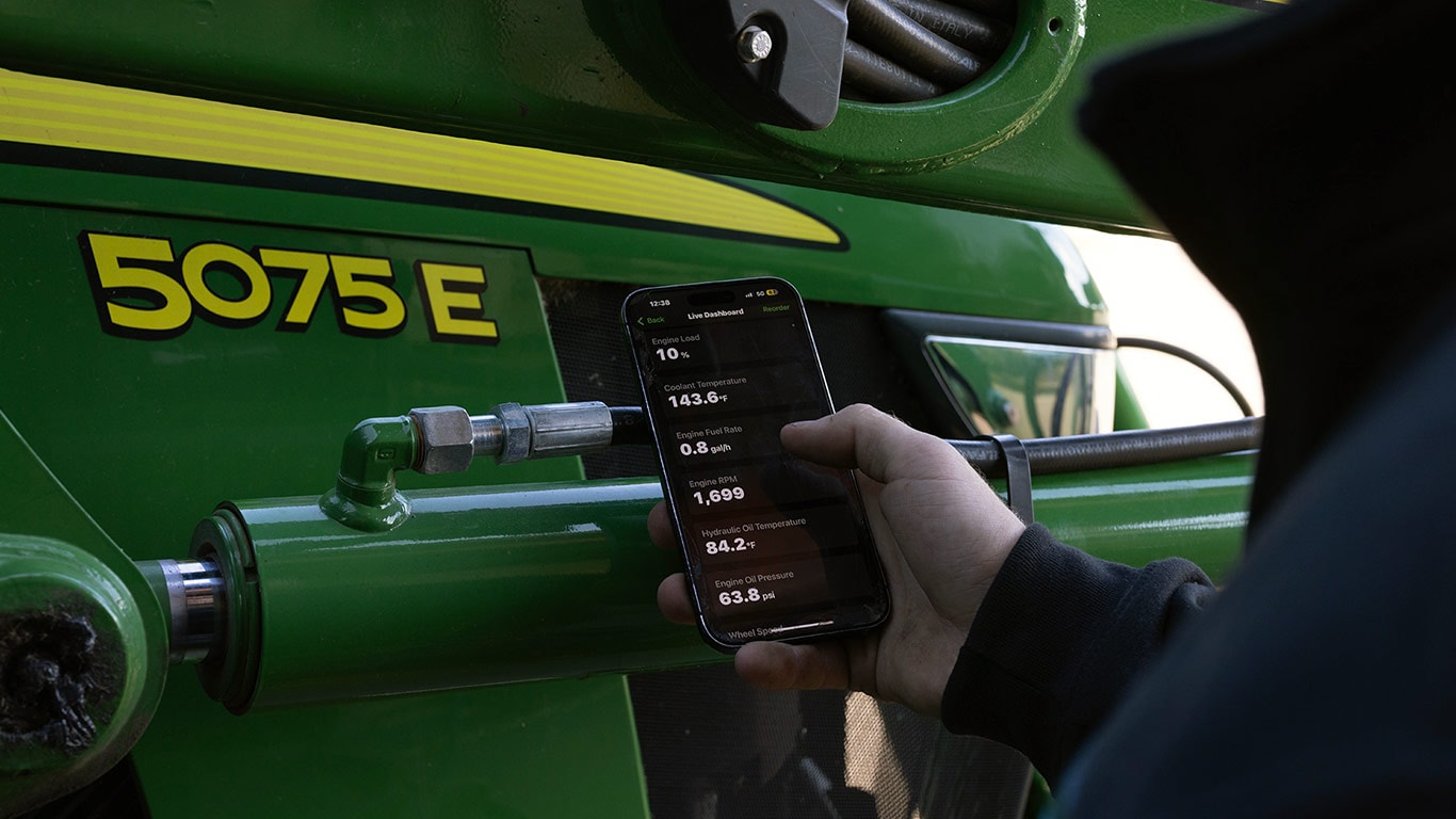 hand holding a cell phone with an app in front of a green and yellow tractor