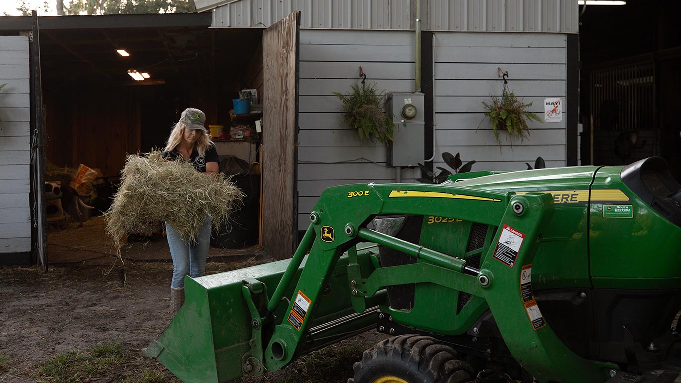 person carrying hay to a green and yellow compact tractor