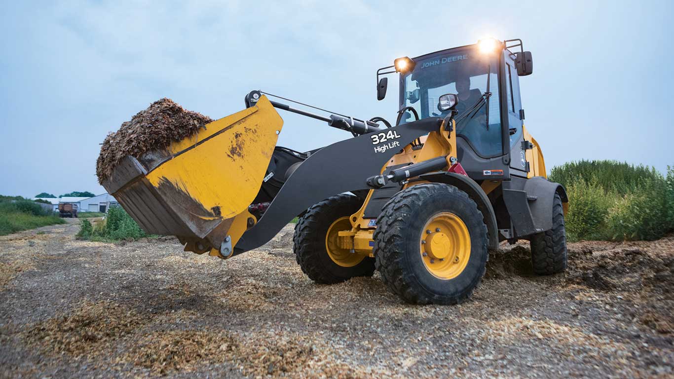 324L mini loader moving debris at dusk with headlights on