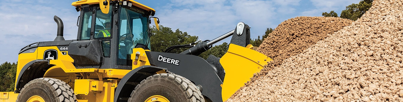 644 X-Tier mid-size four-wheel-drive loader scooping with its bucket in a pile of rocks with a blue sky in the background