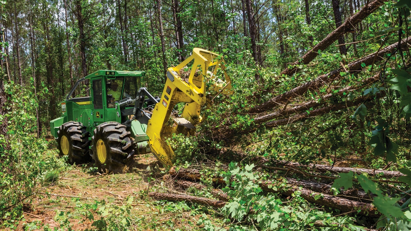 John Deere 643L Wheeled Feller Buncher lifting cut logs in the forest.