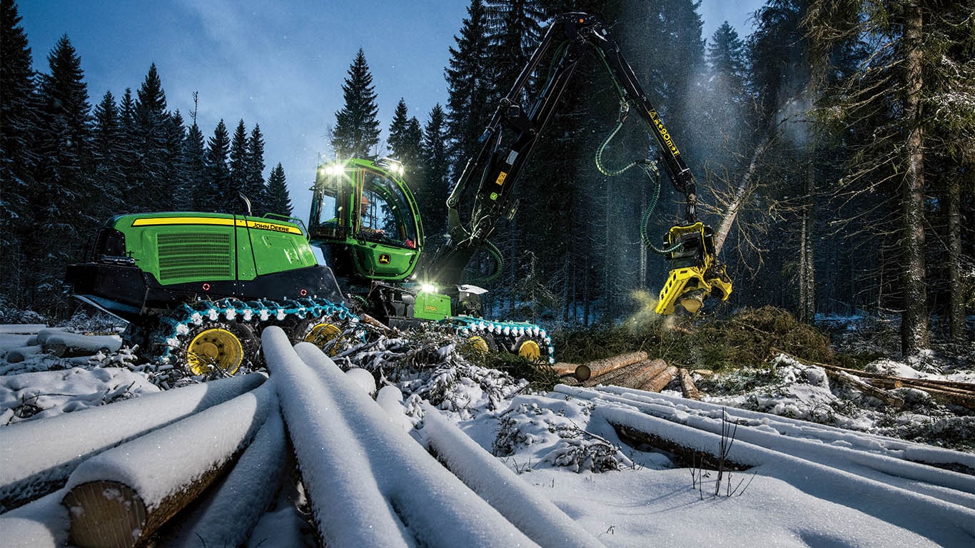 A John Deere wheeled harvester preparing to fell a tree in a forest.