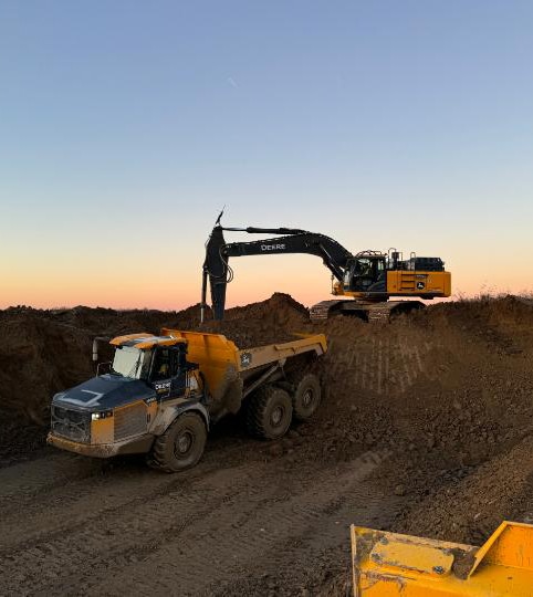 John Deere excavator loads dirt into a John Deere articulated dump truck at a construction site