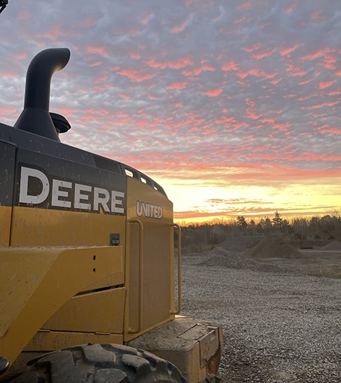 A John&nbsp;Deere wheel loader at rest, bathed in the warm glow of a setting sun