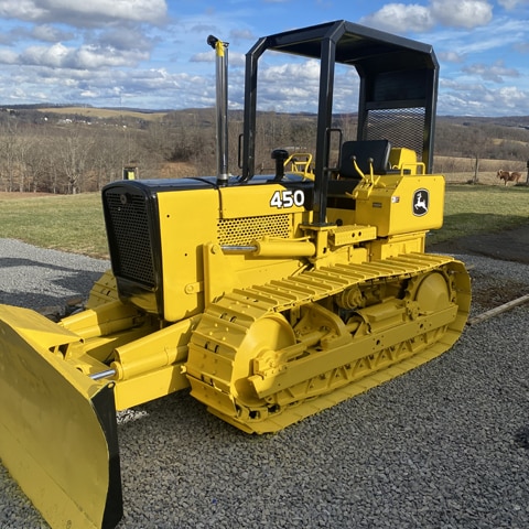 A John Deere 450 G Crawler Dozer sitting on gravel with rolling hills in the background.