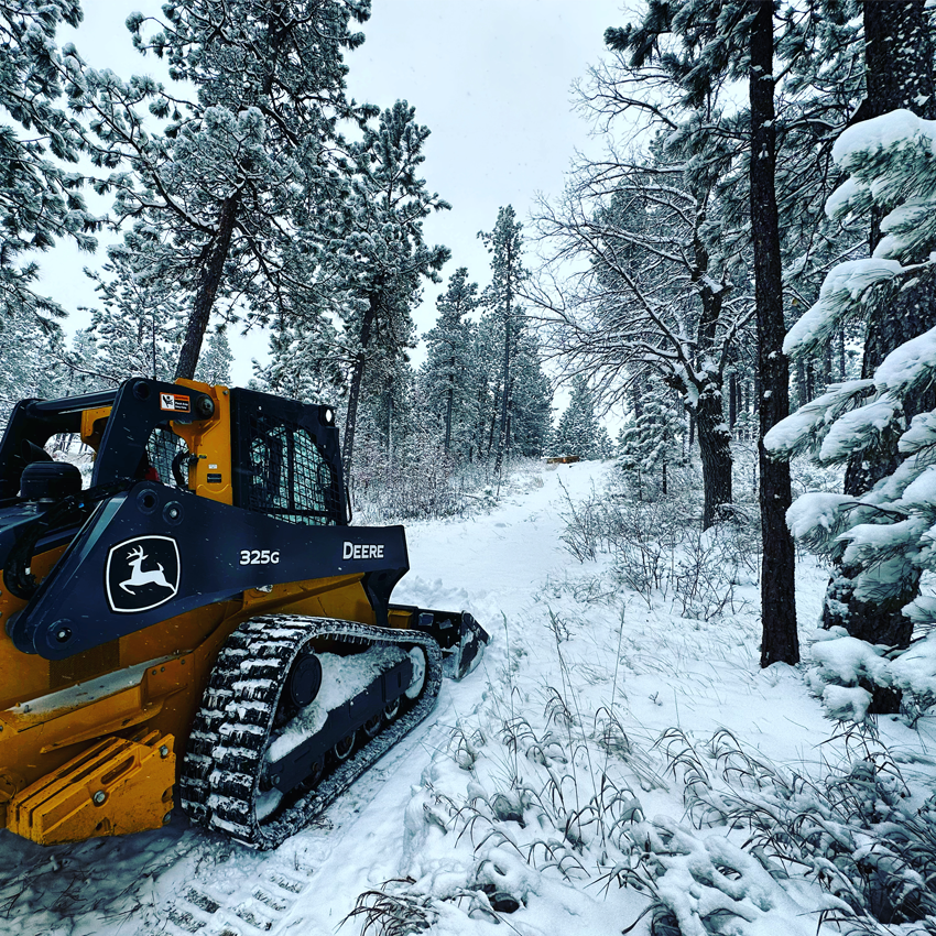 John Deere 325G Skid Steer driving through snow.