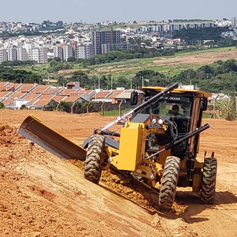 A Motor Grader leveling an incline with residential houses in the background.