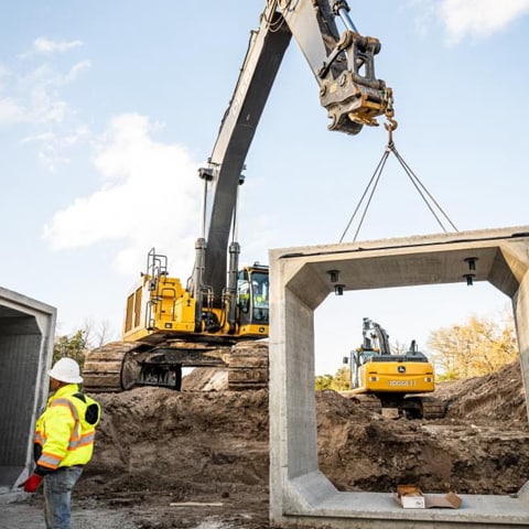 A John Deere Excavator laying concrete bricks for underground drainage.